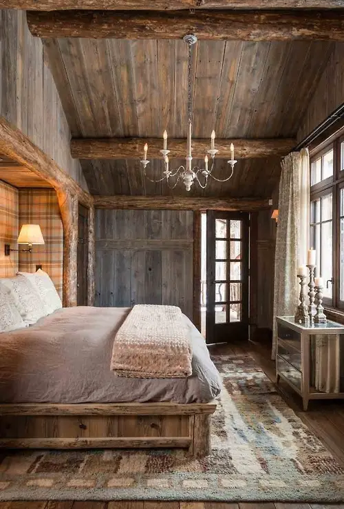 Watm and cozy rustic bedroom with a simple chandelier light fixture.  Love the vaulted ceiling, barn door wall, and over all design.