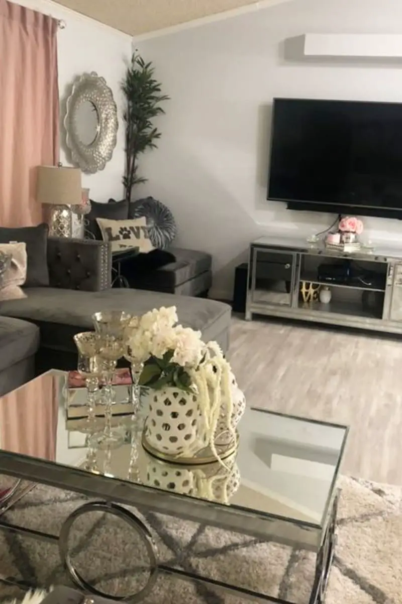 Grey living room with neutral wood floors, mirror topped coffee table, cosy u-shaped grey couch and farmhouse style entertainment center