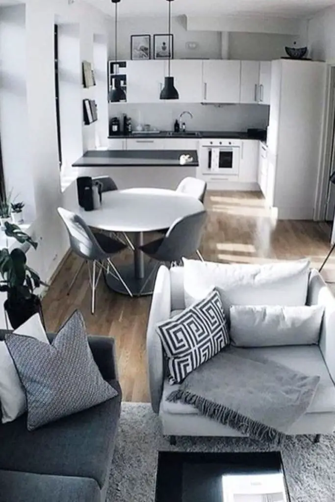grey living room inside a tiny house with open floor plan showing modern white kitchen and eating area with neutral wood floors throughout