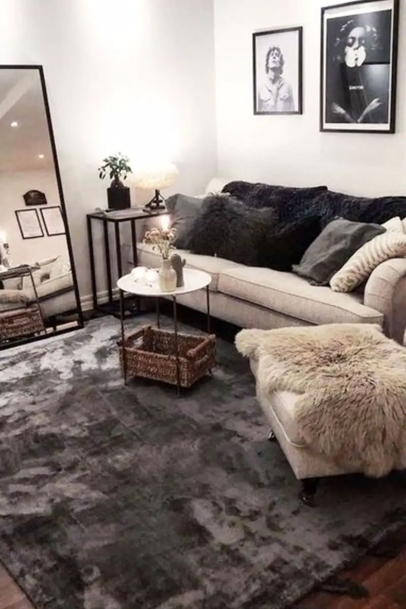 Small living room with neutral tan couch, light grey and dark grey accent throw pills, fur throw blanket, dark grey accent area rug and big mirror against wall