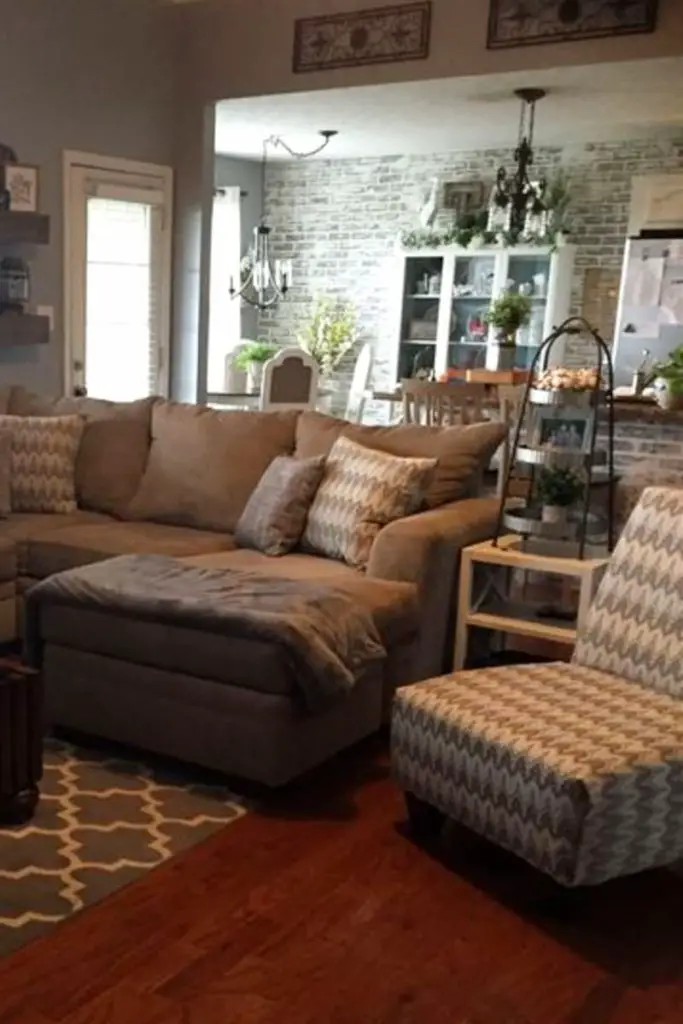 Neutral grey living room with patterned accent chair and throw pillows, grey and white area rug and brick accent wall