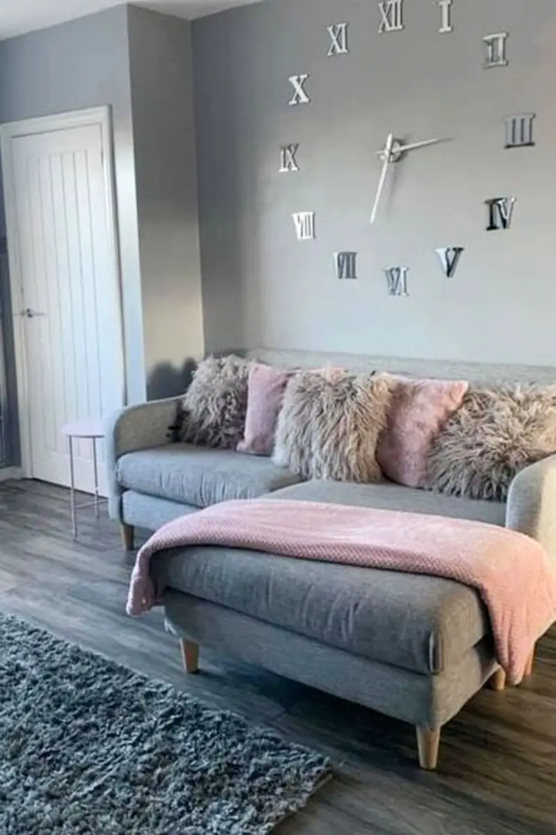 small cosy grey living room couch with lounge, textured throw pillows for pops of color and large wall clocok on wall behind sofa