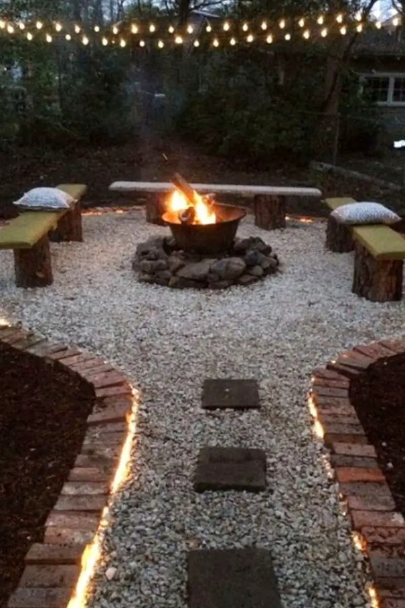 DIY stump seating area around backyard fire pit with gravel ground cover and brick paver walkway