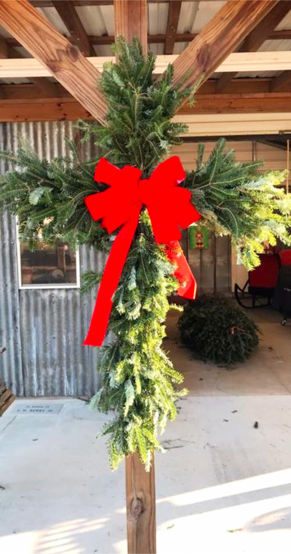 Evergreen cross-shaped wreath hung outside on porch with a big red bow.