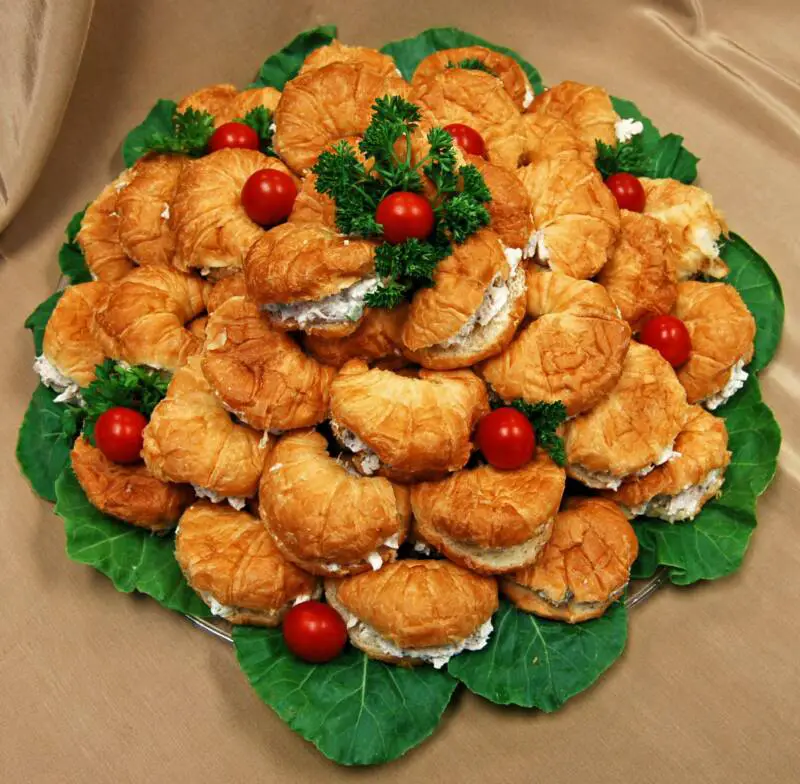 croissant rolls with chicken sales on a platter lined with lettuce on the food buffet table at office party