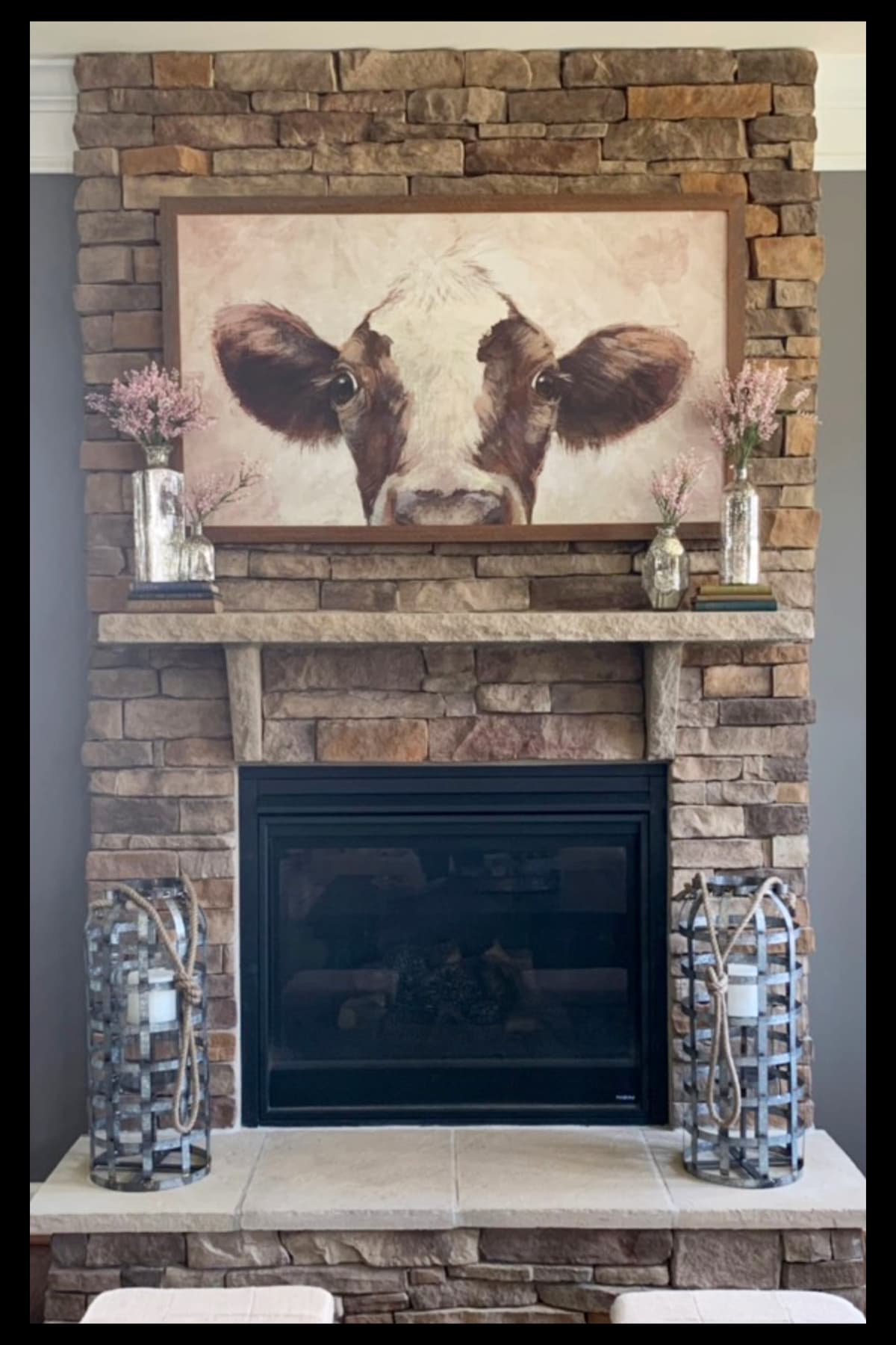 farmhouse fireplace ideas with cow picture on wall, candles on hearth and rustic decor on mantel